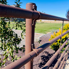 Rust-colored metal railing with a blurred background of greenery and a clear sky.
