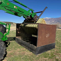 Green excavator lifting hay into a metal container with mountains in the background